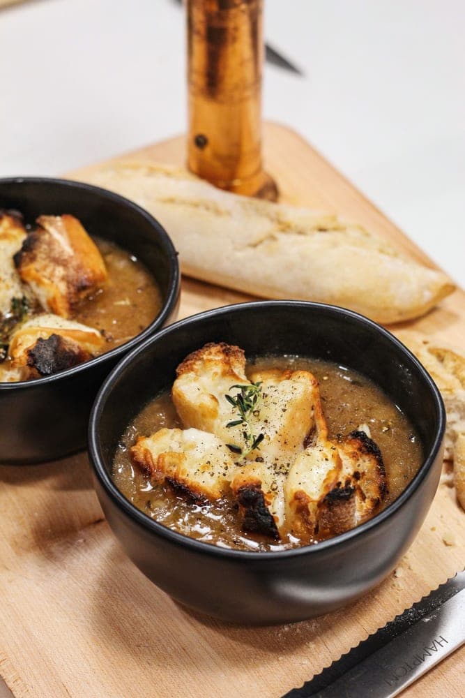 Une soupe à l'oignon gratinée, croûtons dorés, avec un morceau de baguette