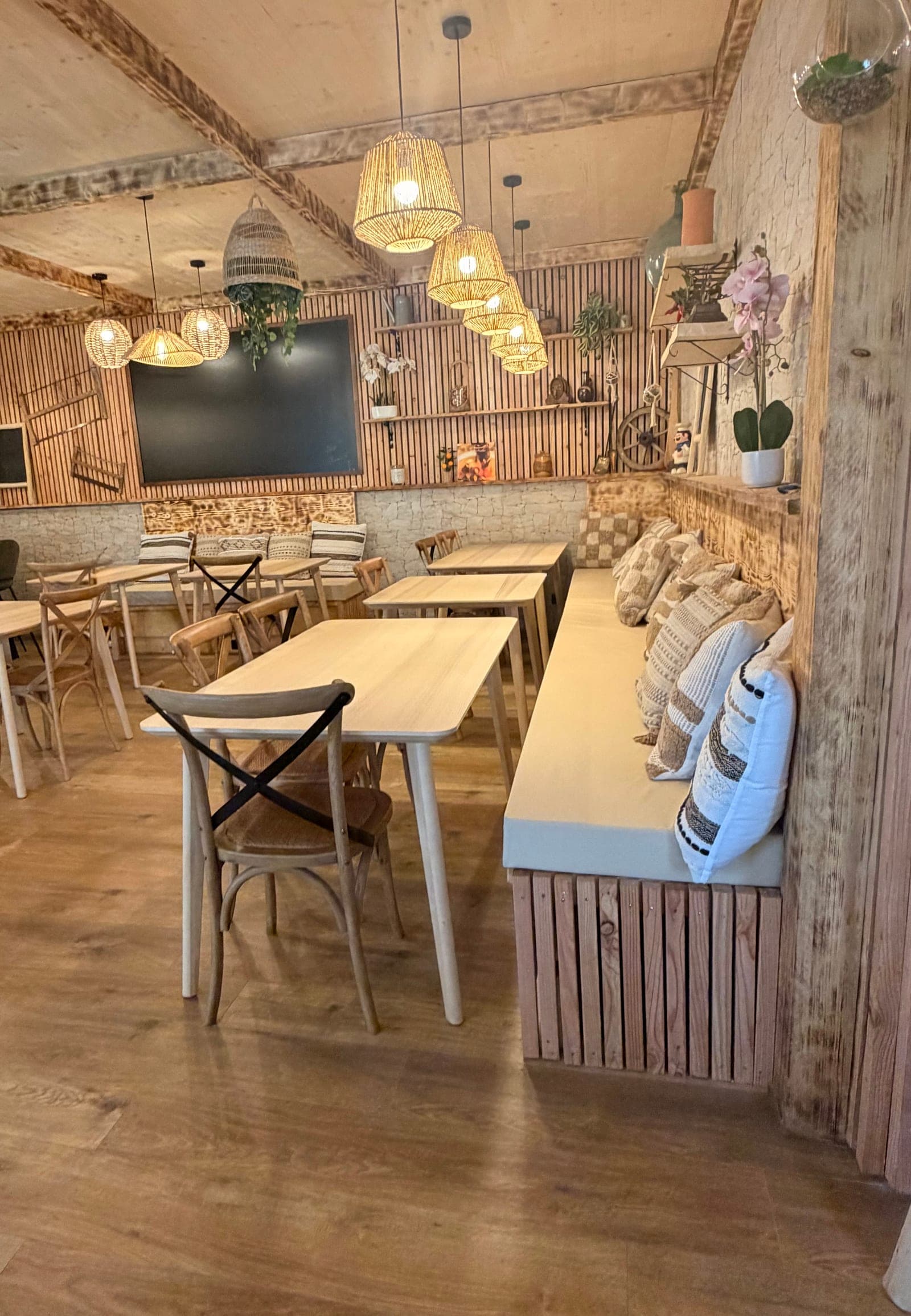 La banquette et ses coussins, les tables et l'ardoise, sous les suspensions en osier